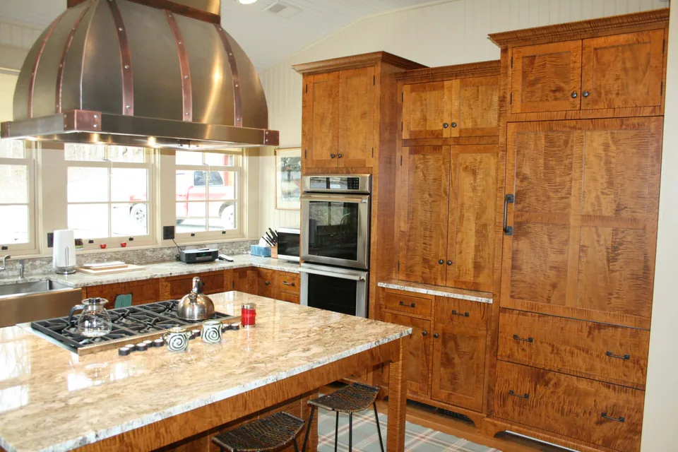 Kitchen with highly figured wood cabinetry and copper-colored straps on a domed hood.