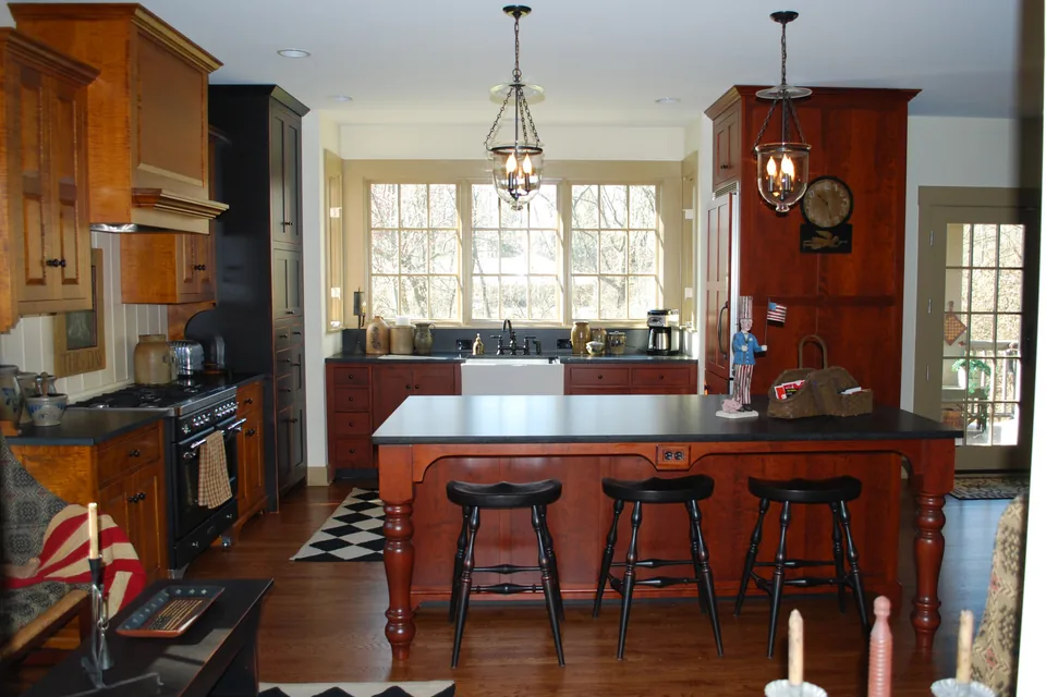 Early American style kitchen with highly figured wood, black-painted accents, and a turned-leg island.