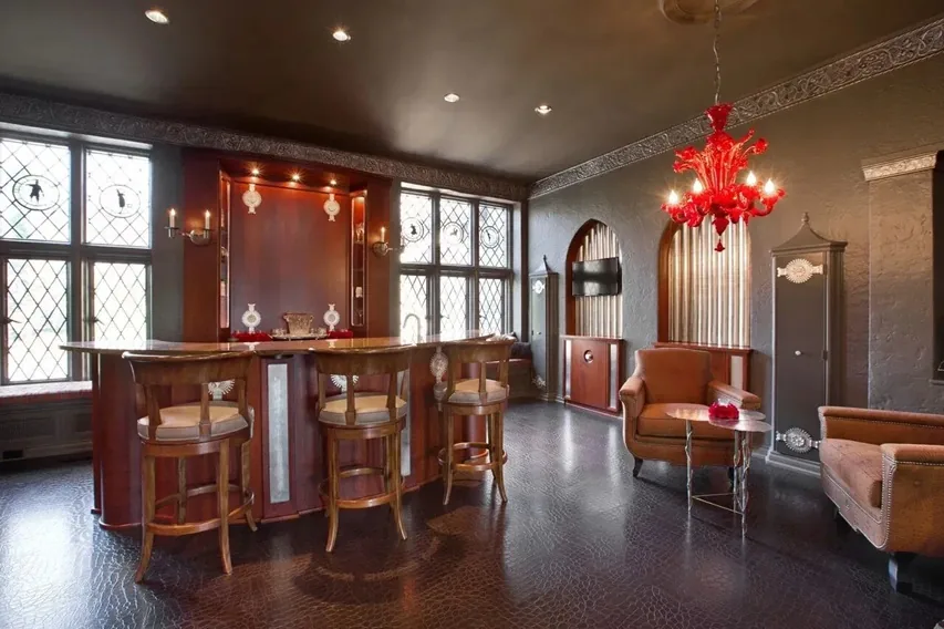 Curved custom bar with a lighted back-bar display cabinet and leaded-glass windows in a historic Tudor interior.