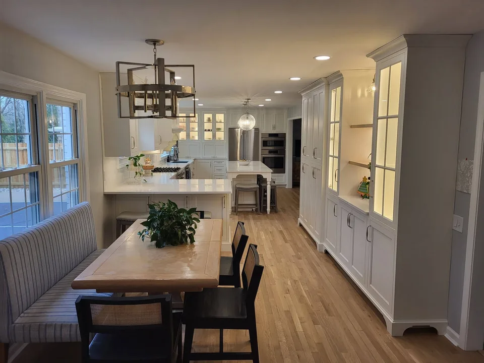 Wall of tall built-in pantry cabinets with a lighted glass-front hutch beside a banquette nook.