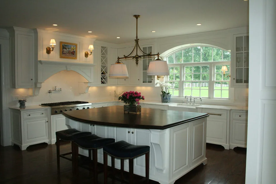 Traditional white kitchen with raised-panel cabinetry, glass display uppers, and a contrasting dark island.