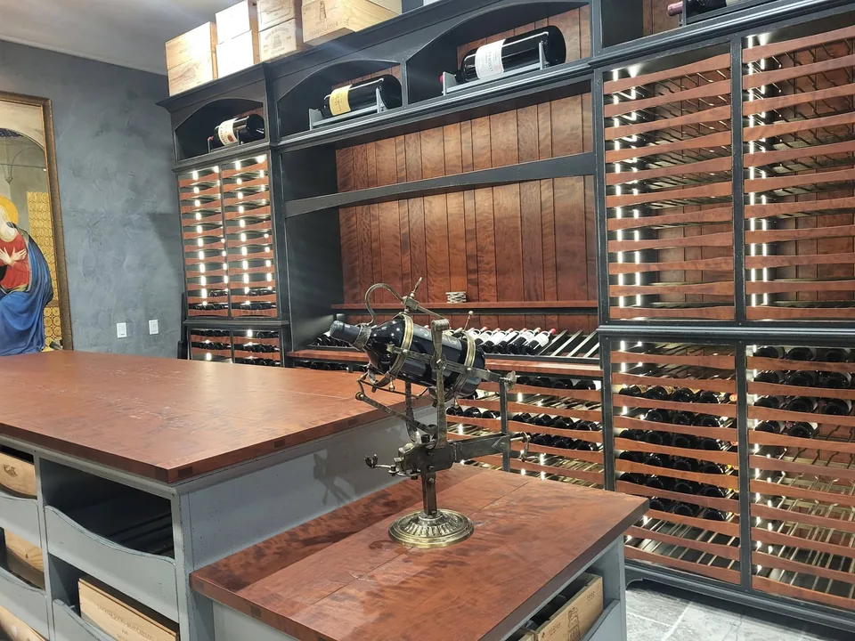 Custom wine cellar tasting island with a stained wood top, backed by floor-to-ceiling dark-painted racking with backlit curved wood slats.